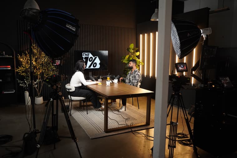 A wide view of the studio: softboxes, cameras on tripods, and two people at the walnut table.