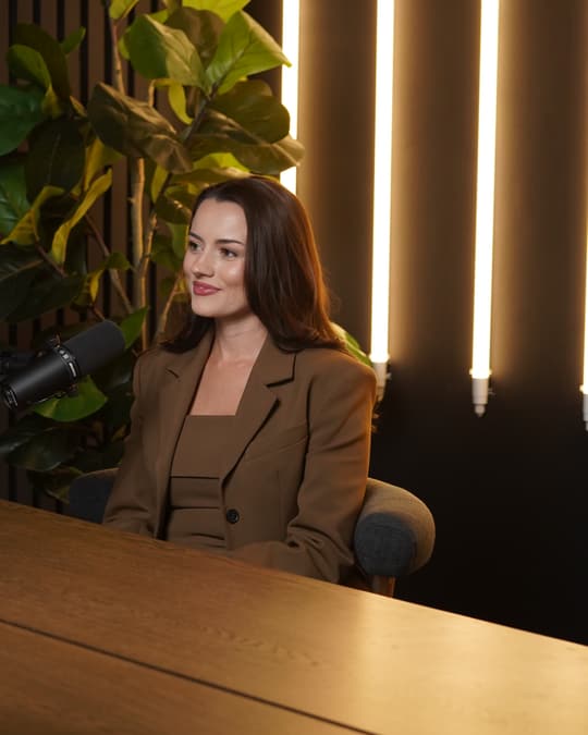 A guest in a brown blazer smiling at the microphone in the studio.